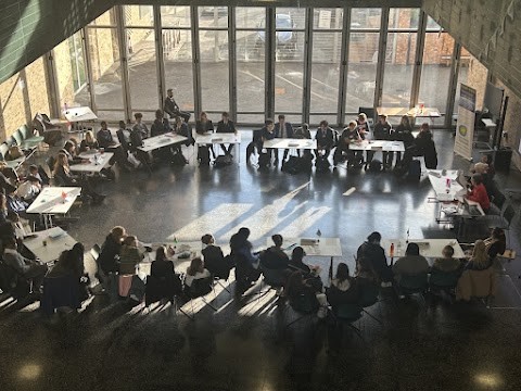 Students seated at tables in large sunny room debating 